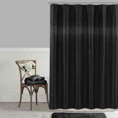 a black shower curtain in a bathroom next to a chair and white flower vase on the floor