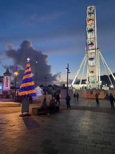 a ferris wheel with a christmas tree in the middle and people walking around it at night