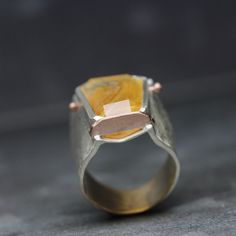 A gorgeous and unique piece of dendritic quartz is the eye catcher in my newest design Golden Flare. The gemstone from Brazil possesses a golden orange color and shows beautiful inclusions. I always challenge myself to come up with designs that are different. I like experimenting with unique stone setting techniques. I fabricated this ring while letting form dictate the outcome. Made from sterling silver and 14k rose gold. A rustic texture (partially hammered and diamond finish) adds a dynamic a Unique Faceted Citrine Jewelry, Unique Citrine Rings With Polished Finish, Unique Citrine Ring With Polished Finish, Dendritic Quartz, Quartz Ring, Silver Pieces, Cleaning Jewelry, Silver Band, Precious Metals