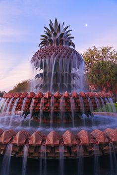 a pineapple fountain with water shooting from it's sides in front of trees