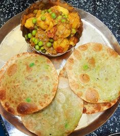 three flat breads on a silver plate next to a bowl of peas and potatoes