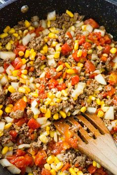 a skillet filled with ground beef, tomatoes and corn next to a wooden spoon