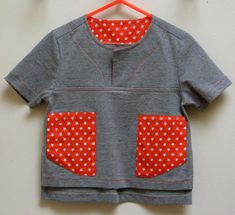 a gray shirt with red and white polka dots on the chest, hanging from a hook