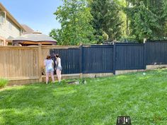 two women are standing in the grass near a fence