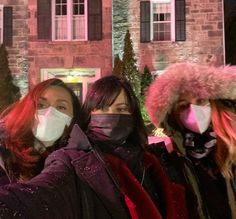 three women wearing face masks standing in front of a house at night with snow on their faces