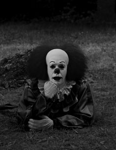 a creepy clown is sitting in the grass