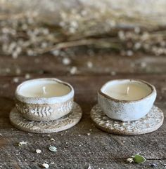 two white tea cups sitting on top of each other next to a cup with a candle in it