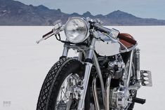 a motorcycle is parked in the middle of an empty desert area with mountains in the background