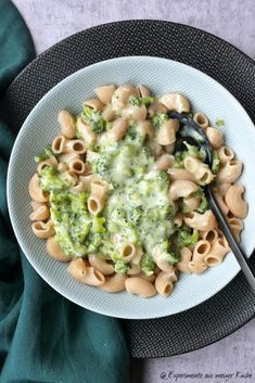 a white bowl filled with pasta and broccoli on top of a black plate