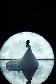 a woman in a white dress is looking at the moon through a circular window with water reflection