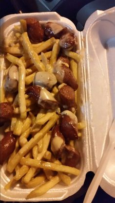 a plastic container filled with french fries covered in cheese and sausages next to a fork