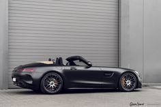 a black mercedes sls roadster parked in front of a garage door with the top down