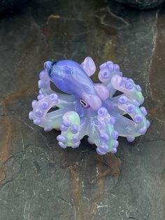 a purple and green toy octopus laying on top of a stone floor next to a rock