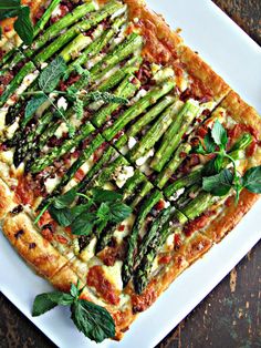 a square shaped pizza with asparagus and cheese on it sitting on a white plate