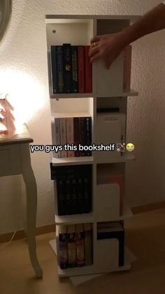 a person reaching for books on top of a book shelf in front of a lamp