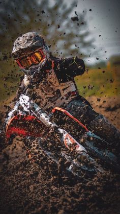 a man riding on the back of a dirt bike down a muddy hill with trees in the background