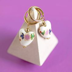 A beautiful pair of white porcelain heart huggie earrings with floral detail. These lovely earrings feature porcelian style ceramic glazed heart with a subtle floral design suspended from gold plated huggie hoops. The earrings would make a lovely gift, treat for yourself and certainly a welcome addition to any jewellery collection. Presented in a an organza gift bag with the sentiment card of your choice. If you would like to upgrade your purchase to include a gift box please order here: https:/ Porcelain Heart, Heart Hoop Earrings, Wedding Keepsakes, Huggie Earrings, Blue Pearl, Pearl Flower, Lovely Earrings, Organza Gift Bags, Jewellery Collection