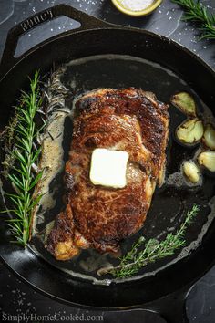 a piece of meat in a skillet with butter on top and some herbs around it