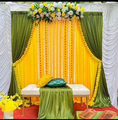 a decorated stage with yellow and green drapes, white flowers and greenery on the wall