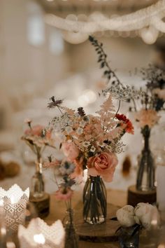 there are many flowers in vases on the table with candles and lights behind them