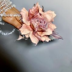 a woman's hand holding a pink flower with chains around it and bracelets on the wrist