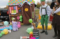 people dressed up in costumes standing around a gingerbread house with balloons and candy on the ground