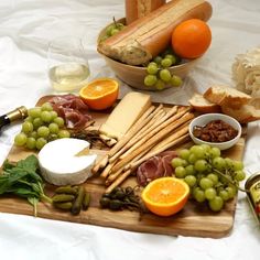 a wooden cutting board topped with cheese, meats and fruit next to bottles of wine