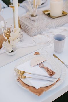 a table set with white plates and silverware, napkins and gold utensils