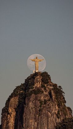 the statue of christ on top of a mountain with a full moon in the background