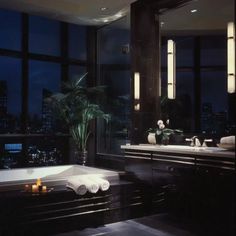 a bathroom with two sinks and a bathtub in front of large windows at night