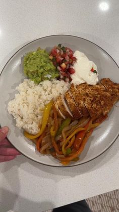 a person holding a plate with rice, chicken and vegetables on it in their hand