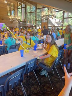 a group of people sitting at long tables in a room filled with blue and yellow chairs