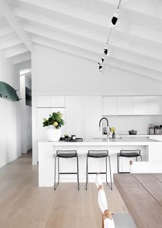 an open kitchen with white walls and wooden floors is pictured in this image, there are three chairs at the center of the room