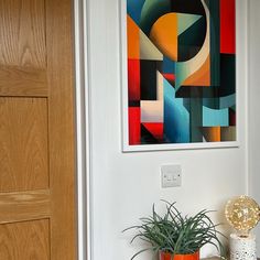 a painting hangs on the wall next to a potted plant in front of a door