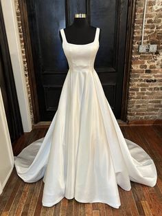 a white wedding dress sitting on top of a wooden floor next to a mannequin