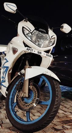 a white and blue motorcycle parked on top of a brick road next to a black car