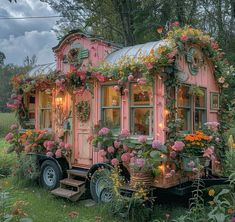 a small pink house with flowers growing on the roof and windows is parked in front of some trees