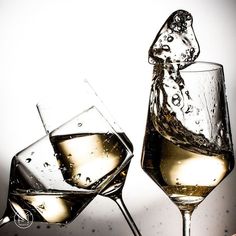 two wine glasses filled with white wine being poured into one glass and the other is half full