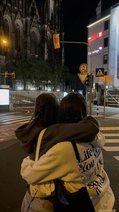 two people are hugging on the street at night