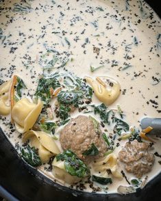 a pot filled with pasta, meatballs and spinach on top of white sauce