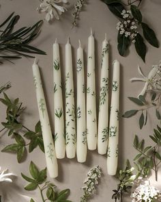 six candles with green leaves and white flowers