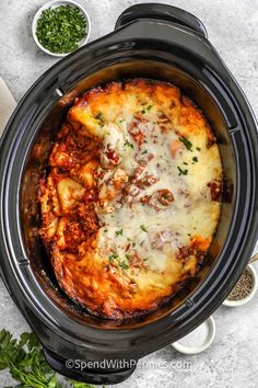 a crock pot filled with lasagna casserole next to some parsley