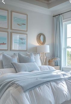 a bedroom with white bedding and paintings on the wall above it, along with two windows