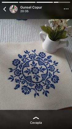 an embroidered tablecloth with blue flowers in a white vase on top of the table