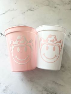 two cups with faces painted on them sitting next to each other in front of a marble counter