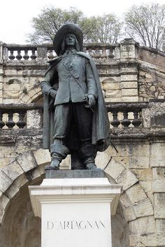 a statue of a man with a hat and coat standing in front of a building