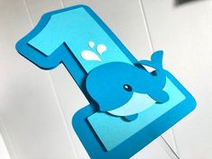 a blue number one shaped like a whale is hanging from a hook on the wall