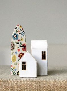 two small white houses sitting next to each other on top of a table with a vase in front of them