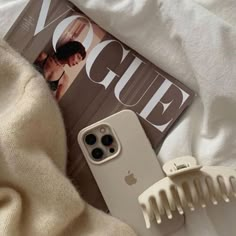 an iphone case sitting on top of a bed next to a hair comb and magazine