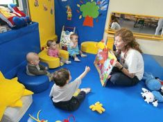 a woman sitting on the floor reading to children in a play room with blue carpet and yellow walls